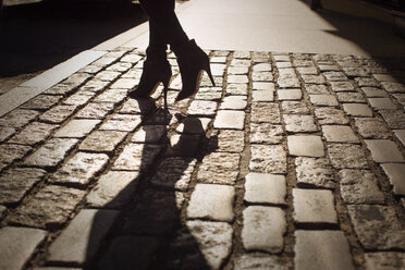 Low section of woman walking on cobblestone during sunset - CAVF04722