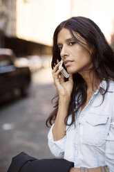 Frau schaut weg, während sie auf der Straße mit ihrem Smartphone telefoniert - CAVF04723