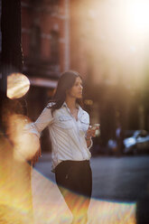 Frau schaut weg, während sie ihr Smartphone auf der Straße hält - CAVF04730