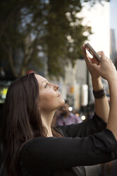 Side view of woman photographing while standing in city - CAVF04731