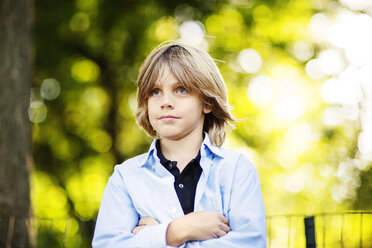 Boy looking away while standing with arms crossed at park - CAVF04763