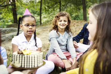 Freunde feiern Geburtstag, während sie auf einer Wiese im Park sitzen - CAVF04768