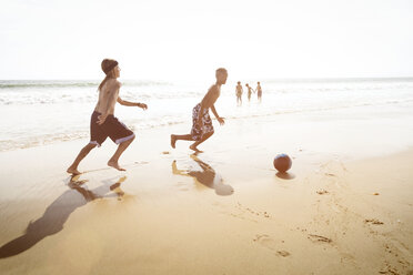Side view of boys playing soccer on beach against clear sky - CAVF04831