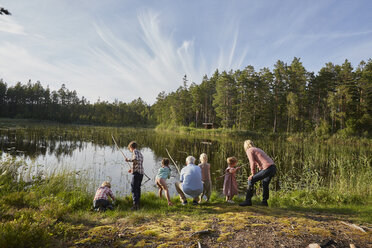 Großeltern und Enkelkinder beim Angeln am sonnigen Seeufer im Wald - CAIF09415