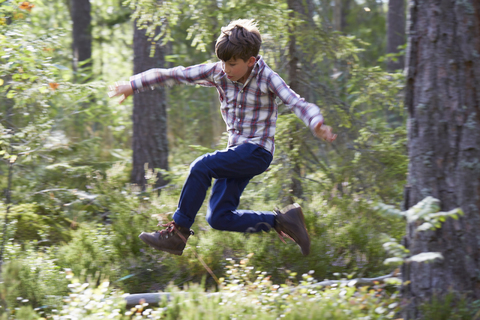 Energiegeladener Junge springt im Wald, lizenzfreies Stockfoto