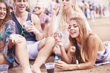 Young friends hanging out blowing bubbles at music festival - CAIF09435