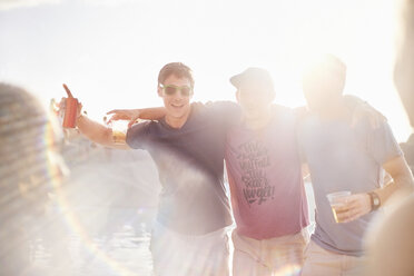 Porträt junger Männer beim Biertrinken auf einer sonnigen Party am Pool - CAIF09437