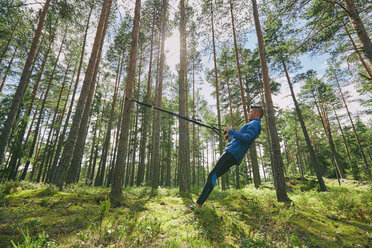 Runner stretching with resistance band on tree in woods - CAIF09467