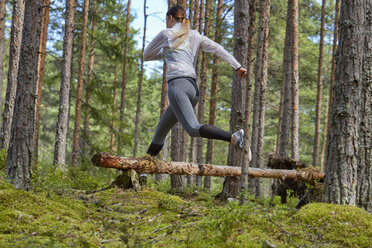 Läufer springt über umgestürzten Baumstamm im Wald - CAIF09469