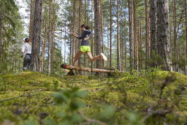 Läufer springt über umgestürzten Baumstamm im Wald - CAIF09471