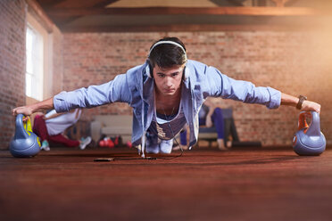 Konzentrierter junger Mann balanciert beim Üben der Plank-Pose auf Kettlebells im Fitnessstudio - CAIF09493
