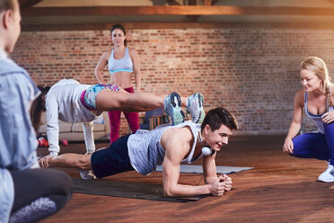 Young man and woman practicing stacked plank pose in gym studio - CAIF09496