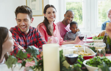 Porträt einer lächelnden Frau, die das Weihnachtsessen mit ihrer Familie am Tisch genießt - CAIF09536
