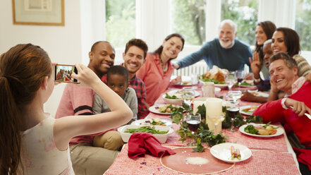 Mädchen mit Fotohandy fotografiert multiethnische Familie am Weihnachtstisch - CAIF09537