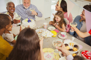 Multiethnische Mehrgenerationenfamilie stößt am Tisch mit Champagner an - CAIF09541