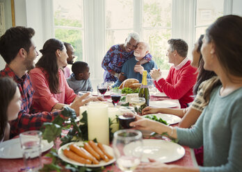 Zärtliches multiethnisches Seniorenpaar, das sich am Weihnachtstisch der Familie umarmt - CAIF09564