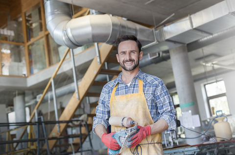 Porträt lächelnder Künstler mit Schleifmaschine im Atelier, lizenzfreies Stockfoto