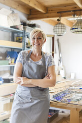 Portrait smiling stained glass artist in studio - CAIF09627