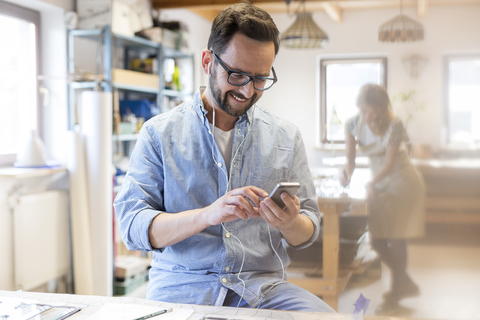 Lächelnder Künstler, der mit Ohrstöpseln und mp3-Player im Studio Musik hört, lizenzfreies Stockfoto