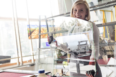 Portrait smiling stained glass artist lifting glass in studio - CAIF09651