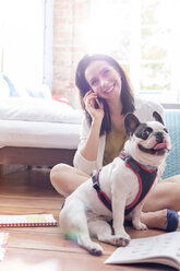 Smiling woman talking on cell phone near French Bulldog on floor - CAIF09657