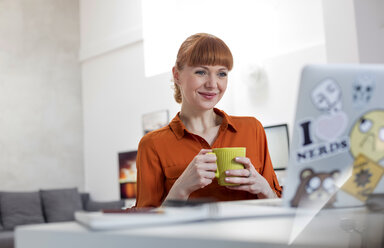 Lächelnde Frau trinkt Kaffee und arbeitet am Laptop - CAIF09659