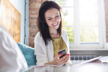 Smiling woman texting with cell phone on bed - CAIF09661