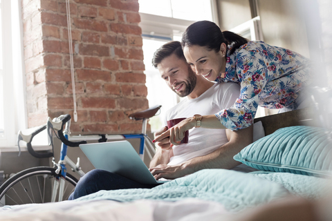 Couple drinking coffee using laptop on bed stock photo