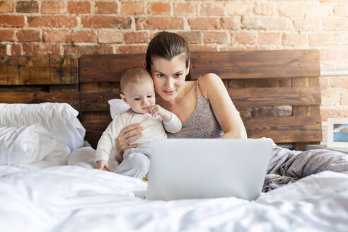 Mutter mit kleiner Tochter benutzt Laptop auf dem Bett - CAIF09686