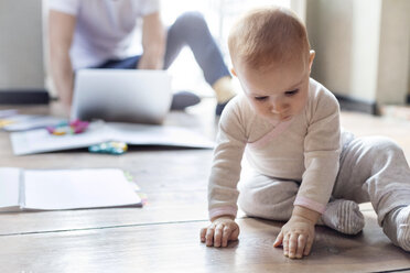 Kleine Tochter sitzt auf dem Boden in der Nähe des Vaters, der am Laptop arbeitet - CAIF09690