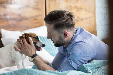 Man petting Jack Russell Terrier on bed - CAIF09693