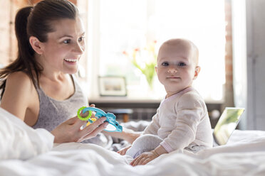 Portrait mother and daughter playing on bed - CAIF09694