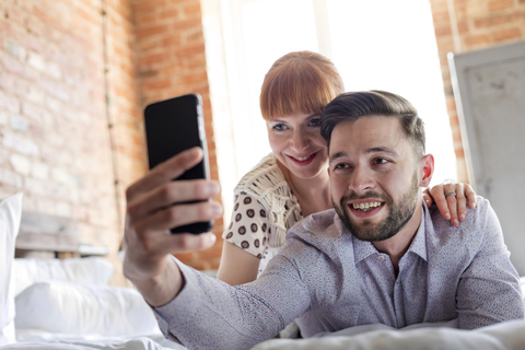 Paar, das auf dem Bett liegt und ein Selfie mit einem Fotohandy macht, lizenzfreies Stockfoto