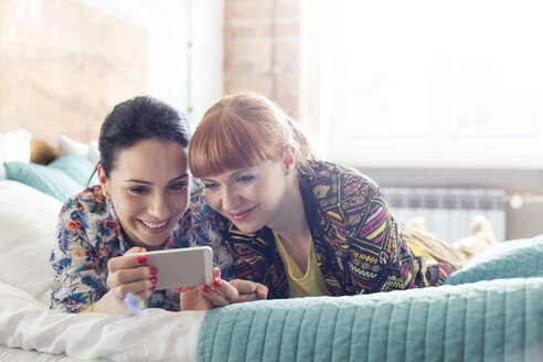 Frauen mit Mobiltelefon auf dem Bett liegend - CAIF09697