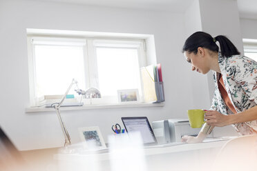 Geschäftsfrau trinkt Kaffee und arbeitet am Laptop im Büro - CAIF09700