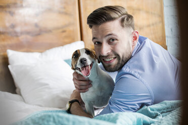 Portrait smiling man petting Jack Russell Terrier dog on bed - CAIF09705