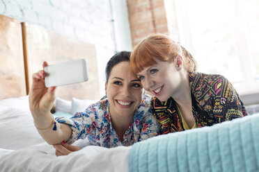 Lächelnde Frauen nehmen Selfie mit Kamera-Handy auf dem Bett liegend - CAIF09707