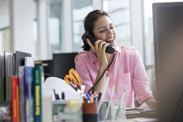 Lächelnde Geschäftsfrau, die am Telefon spricht und am Computer im Büro arbeitet - CAIF09712