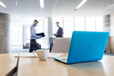 Laptop und Kaffeetasse auf einem Konferenzraumtisch mit Geschäftsleuten im Hintergrund - CAIF09733