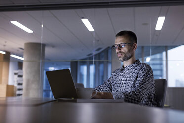 Businessman working late at laptop in office - CAIF09735