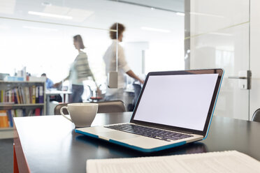 Laptop und Kaffeetasse auf dem Schreibtisch mit Geschäftsleuten, die im Hintergrund laufen - CAIF09736