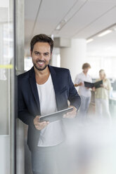 Porträt eines lächelnden Geschäftsmannes, der ein digitales Tablet im Büro hält - CAIF09737