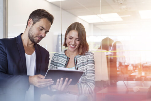 Lächelnde Geschäftsleute, die ein digitales Tablet im Büro benutzen - CAIF09739