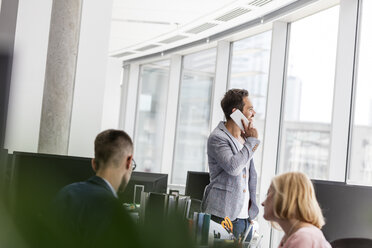 Businessman talking on cell phone at office window - CAIF09744