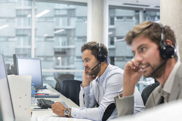 Businessmen with hands-free devices talking on telephone working at computers in office - CAIF09756