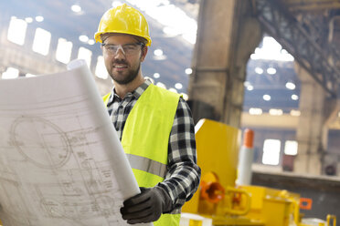 Porträt eines lächelnden Ingenieurs mit Bauplänen in einer Stahlfabrik - CAIF09783