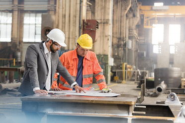 Manager and steel worker engineer reviewing blueprints in factory - CAIF09784