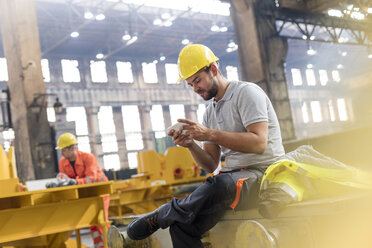 Stahlarbeiter, der während einer Pause in der Fabrik mit seinem Handy SMS schreibt - CAIF09790