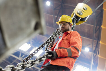 Steel worker holding crane chain in factory - CAIF09806