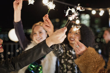 Junge Frauen winken mit Wunderkerzen auf einer Dachterrassenparty - CAIF09824